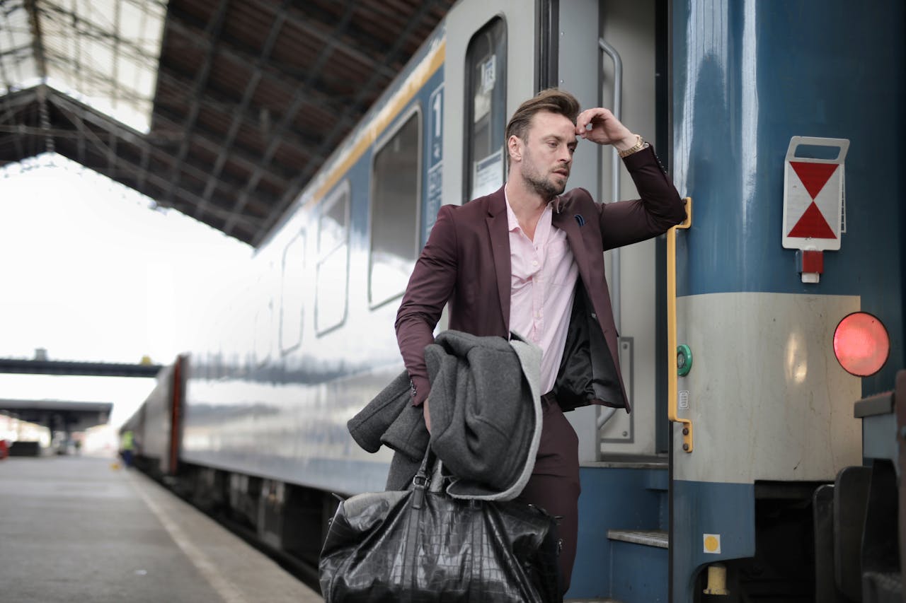 services-06 A man in a suit, carrying bags, looks stressed as he boards a train at a railway station.