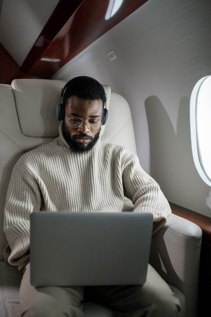 about-us A focused businessman using a laptop and headphones while traveling on a private jet.